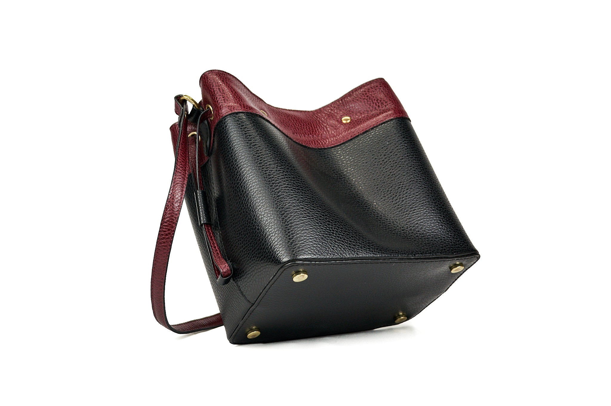 Detalle del inferior del bolso bucket VALDÉZ, en cuero negro y vino tinto, con apoyapies metálicos.