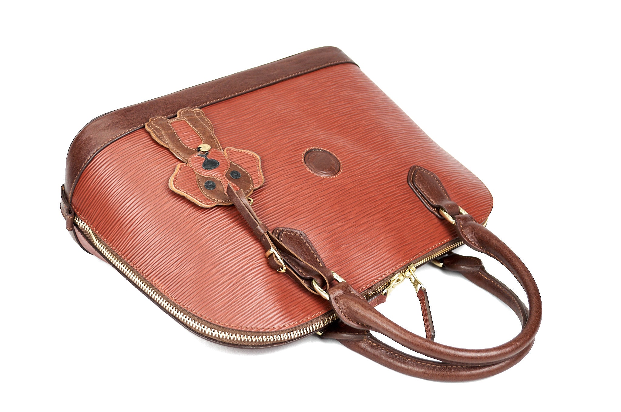 Detalle del bolso de cuero cognac PERRITO acostado, mostrando asas, textura y charm de perrito.
